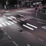 cars driving fast through an intersection at night